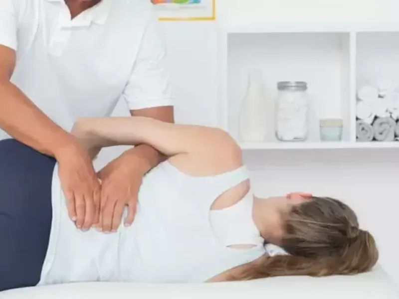 A therapist working on the lower back of a woman lying on her side on a treatment table