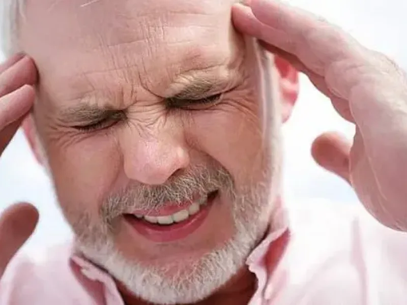 A man with his eyes shut pressing both hands to his temples in pain