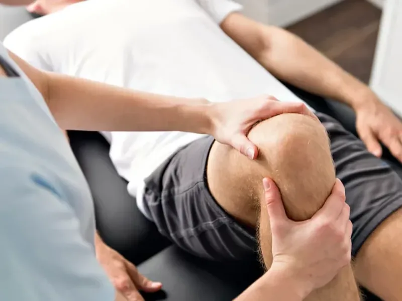 A therapist holding a patient&rsquo;s knee in both hands during a hands-on assessment