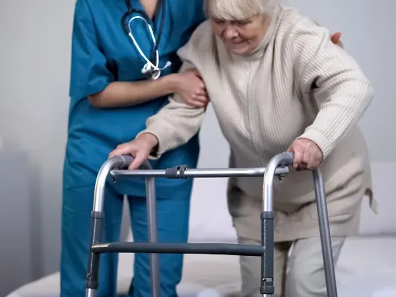 A nurse in scrubs helping an older woman steady herself on a walker