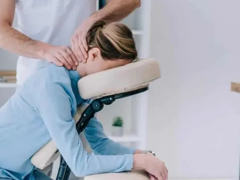 A therapist gently massaging the neck of a woman resting on a massage chair