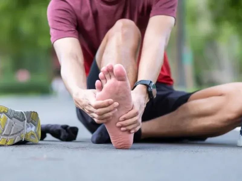 A man sitting on a road holding the bottom of his bare foot in both hands