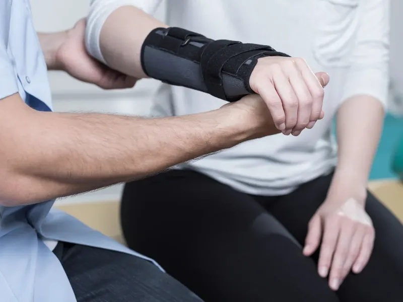 A therapist supporting a patient&rsquo;s forearm, which is wearing a black wrist brace
