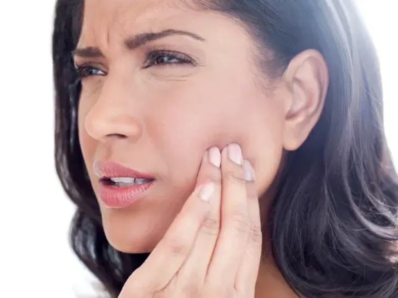 A woman wincing as she presses her fingers against her jaw