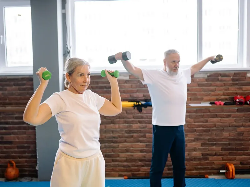 Two older adults exercising with light dumbbells