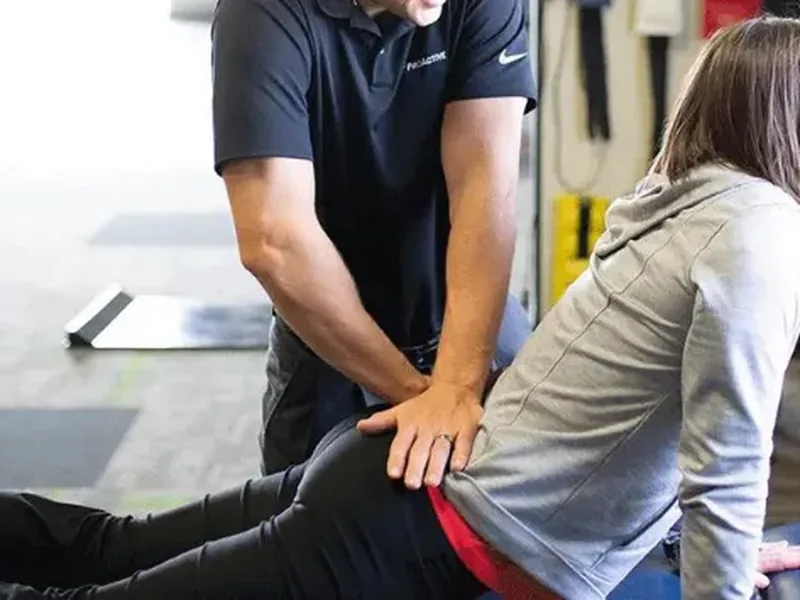 A therapist placing both hands on a patient&rsquo;s lower back as she leans forward on a treatment table