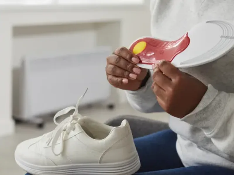 A person holding a shoe insole beside a white sneaker