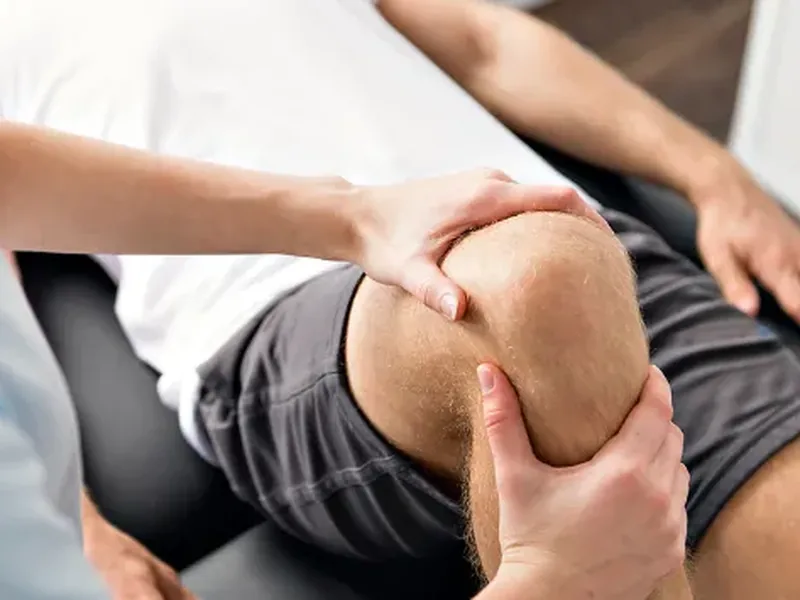 A therapist holding a patient&rsquo;s knee in both hands during hands-on soft tissue work