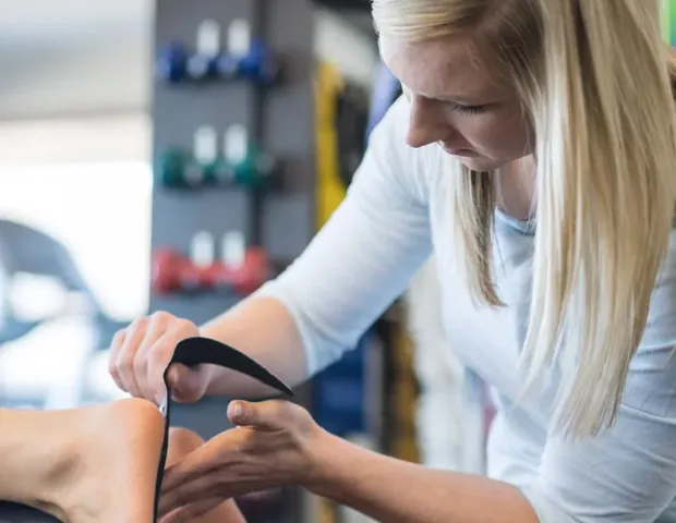 A physical therapist wrapping tape around a patient&rsquo;s foot during hands-on treatment